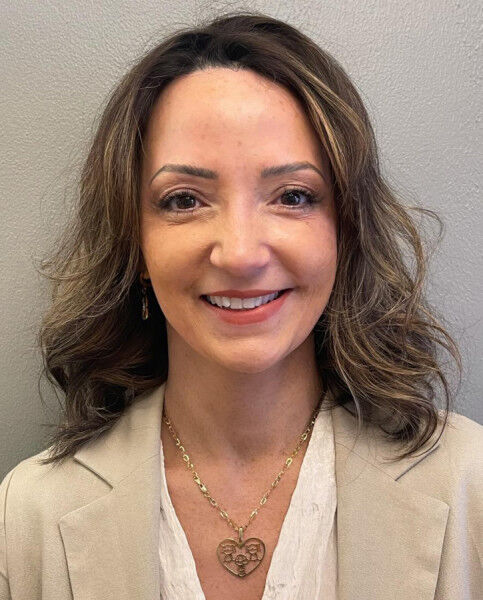 Lawyer Luana Lacerda with shoulder-length wavy hair smiles, wearing a beige blazer and a heart-shaped necklace.