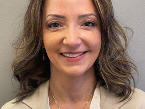 Lawyer Luana Lacerda with shoulder-length wavy hair smiles, wearing a beige blazer and a heart-shaped necklace.