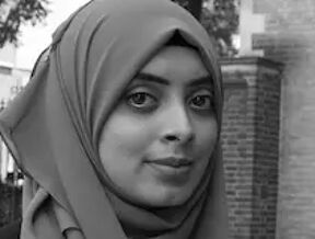 A black and white photo of Saadia Sharmin in a hijab standing on a footpath.