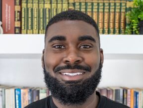 Romain Muhammad standing in front of a bookshelf.