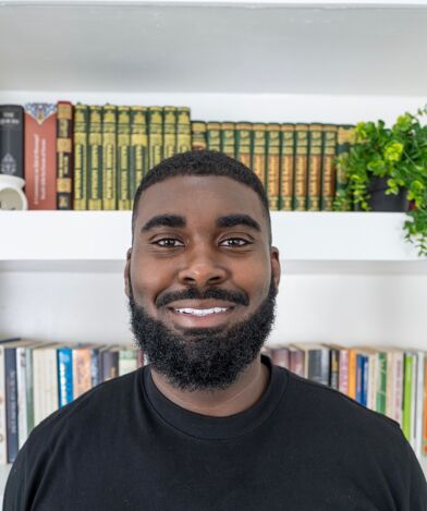 Romain Muhammad standing in front of a bookshelf.